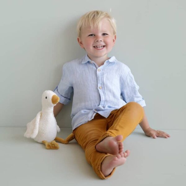 petit garçon assis qui sourit avec sa peluche oie