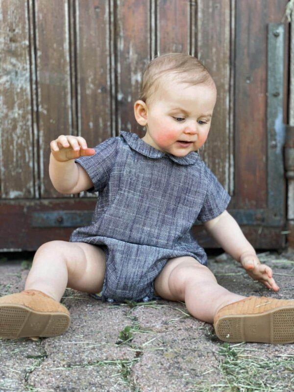 petite fille assise en extérieur portant une barboteuse en double gaze de coton gris chiné de la marque janne mill